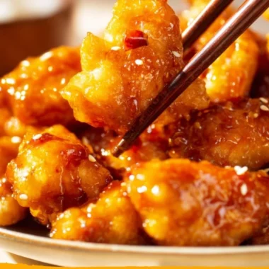 Crispy orange chicken served with vibrant orange sauce and garnished with green onions.