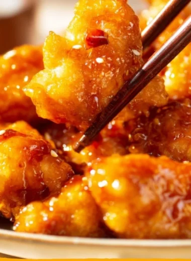 Crispy orange chicken served with vibrant orange sauce and garnished with green onions.