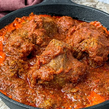 Bowl of Nigerian beef stew with vegetables and spices, showcasing rich flavors.