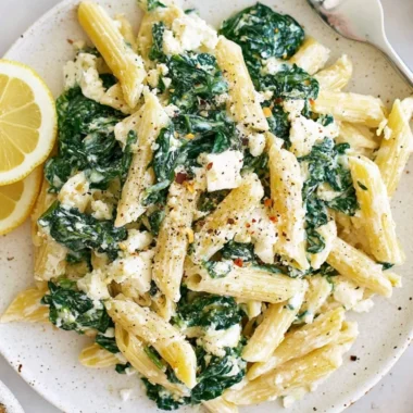 A plate of spinach feta pasta garnished with fresh spinach and feta cheese.