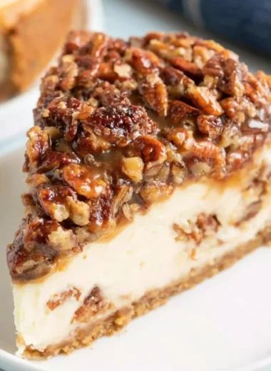 Delicious pecan pie cheesecake topped with pecans and caramel drizzle
